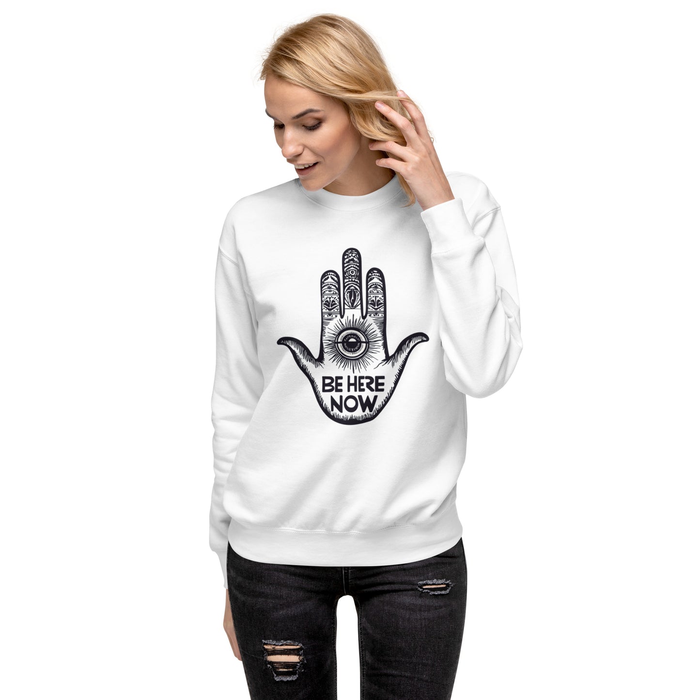 Woman wearing a white sweatshirt featuring a Hamsa Hand design with an evil eye and "Be Here Now" message for mindfulness and style