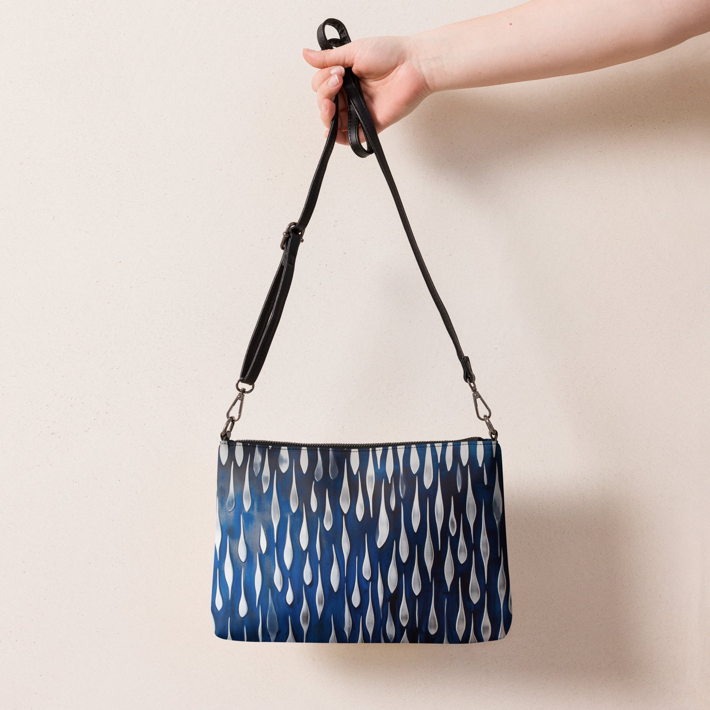 Hand holding a stylish blue crossbody bag with a unique teardrop design and adjustable strap.