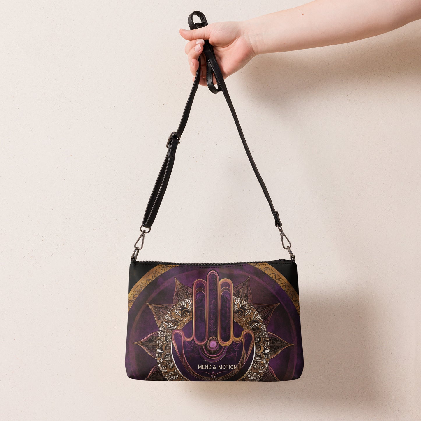 Hand holding a crossbody bag featuring a purple mandala and hamsa design, emphasizing intricate spiritual artwork