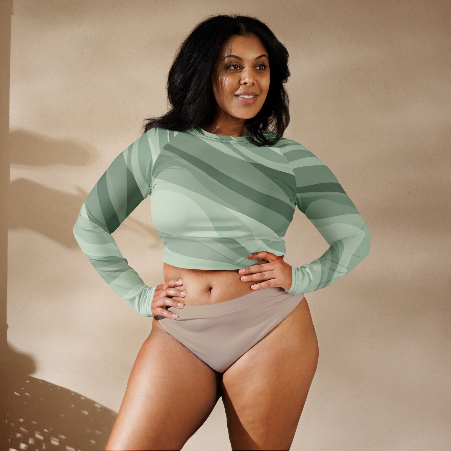 Woman wearing a green long sleeve crop top with abstract wave patterns, hands on hips.