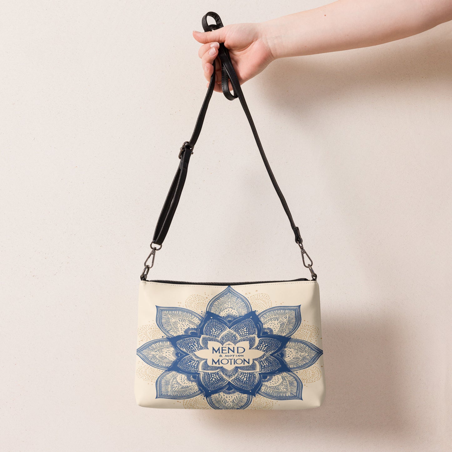 Beige crossbody bag featuring a detailed blue mandala design and "Mend & Motion" text, held by a hand with a black adjustable strap