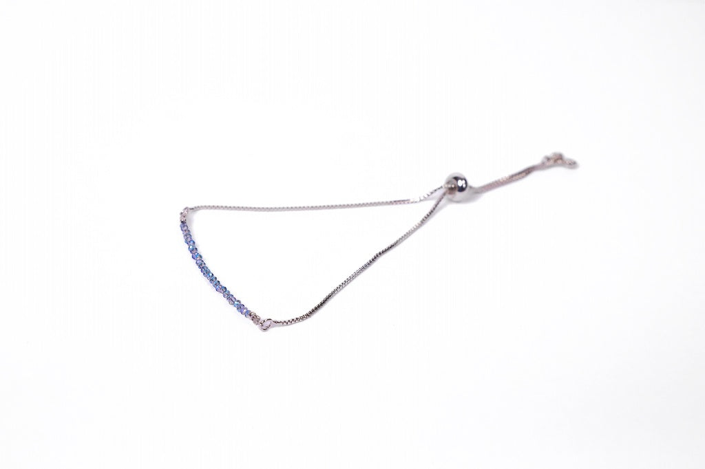 A delicate silver bracelet with an adjustable clasp, featuring a row of small blue beads, displayed against a white background.