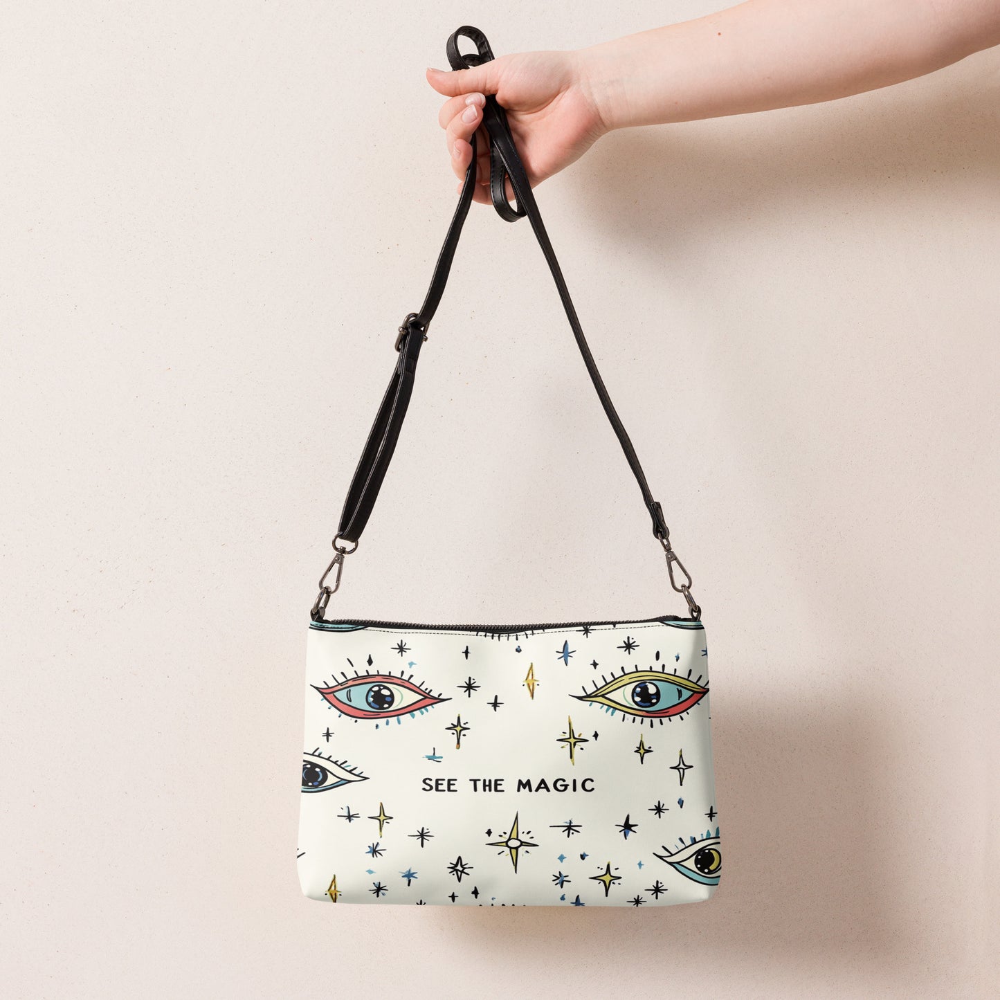 Crossbody bag featuring an eye and star pattern with the text "See the Magic," held by a hand with a sleek black strap design