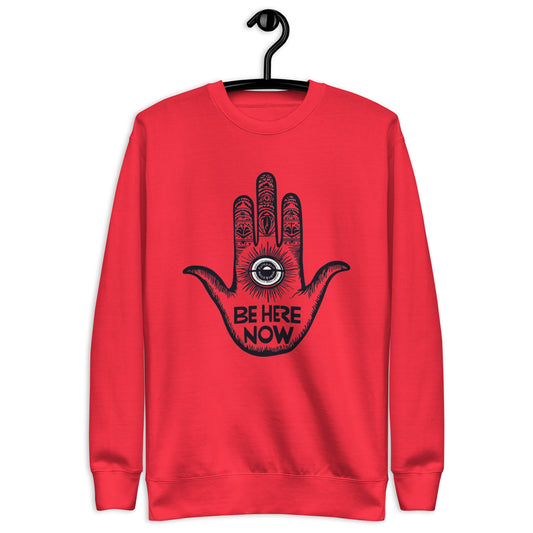 Red sweatshirt featuring a hand design with intricate patterns and the phrase 'Be Here Now' at the center
