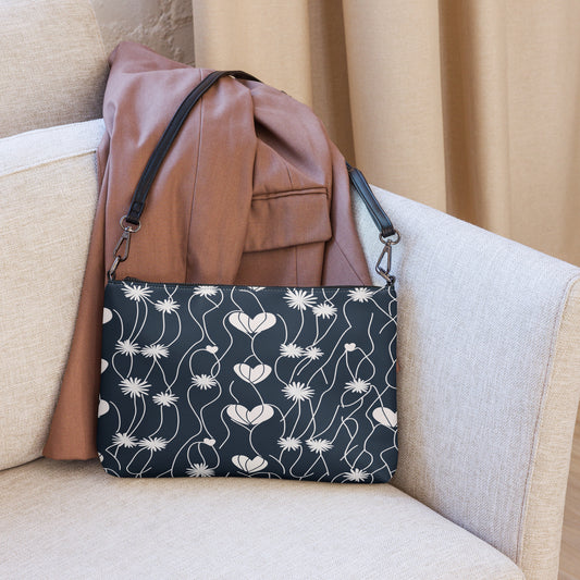 Black crossbody bag with white floral heart pattern placed on a chair with a brown blazer.