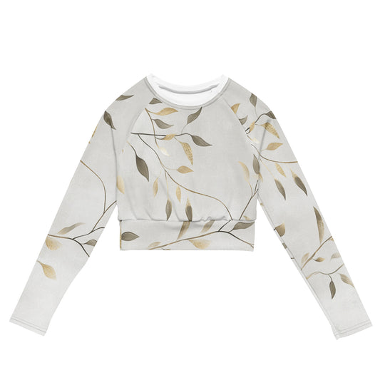 Front view of a long-sleeve recycled crop top with an elegant green and gold leaf pattern on a soft beige background.