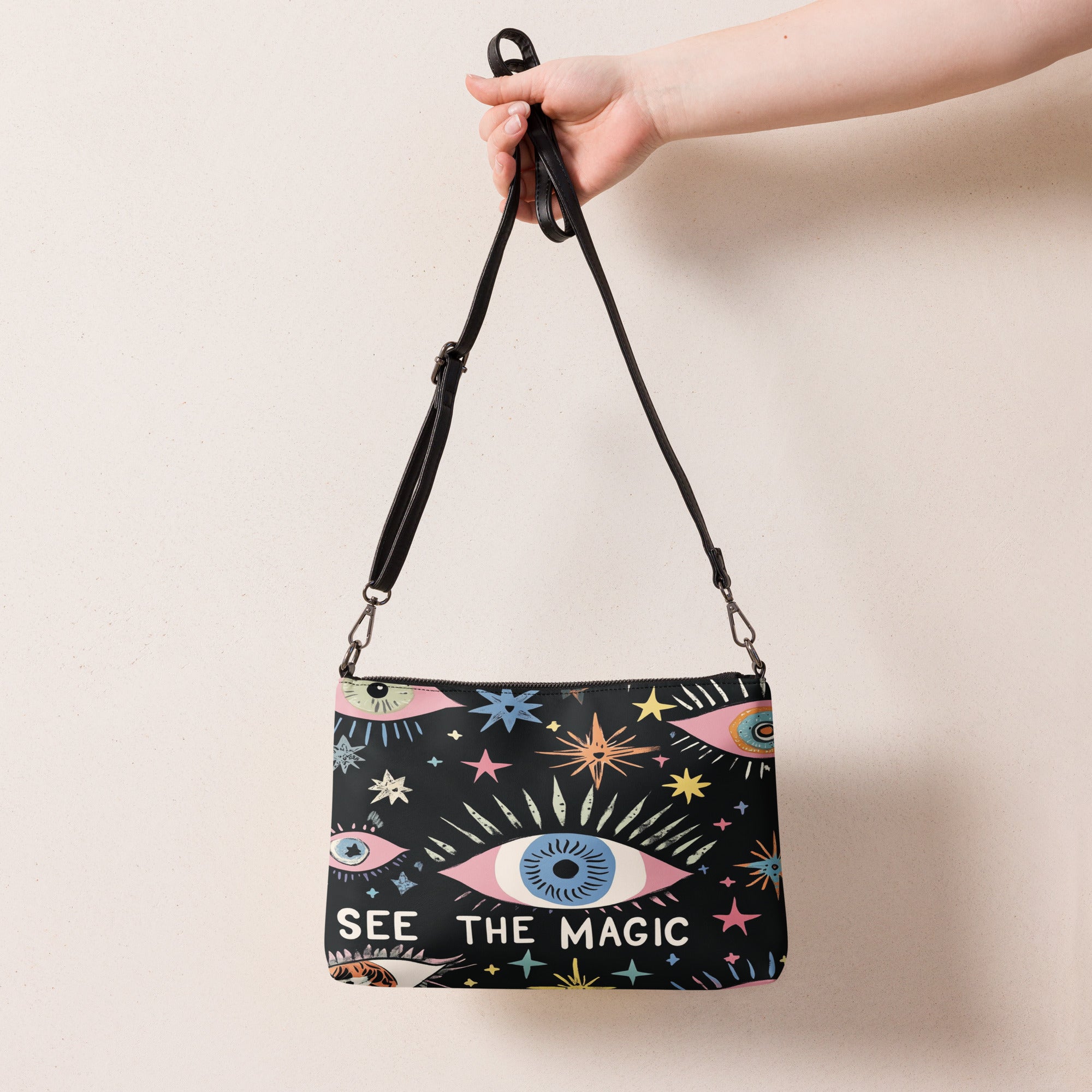  A black crossbody bag featuring colorful eye and star designs with the phrase 'See the Magic' on the front